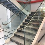Internal feature staircase under construction, with double stringers, full risers, concrete filled tray treads, frameless glass balustrade and stainless steel rails