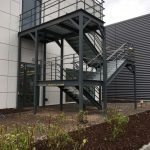External steel staircase, powder coated RAL 7012 with top+mid rail balustrade, stainless steel handrail and Elefant grating treads